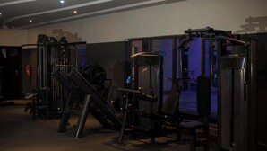 A gym with various exercise machines, a fire extinguisher, and a door with a glass panel. - Gio & Gee Hotels  (Benin City)