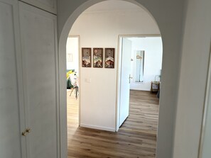 Ein Flur mit Holzboden, einer weißen Tür und einem gerahmten Kunstwerk an der Wand.