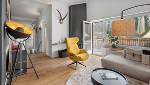 A modern living room with a sofa, a yellow chair, a round coffee table, a lamp, and a large window with a view of the outdoors.