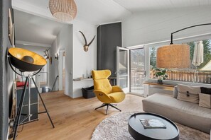 A modern living room with a sofa, a yellow chair, a round coffee table, a lamp, and a large window with a view of the outdoors.
