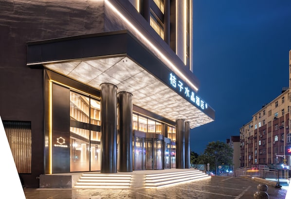 A modern hotel entrance with illuminated signage, large pillars, and a glass facade.