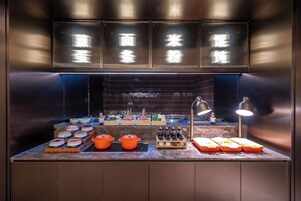A kitchen counter with various cooking utensils and appliances, a display of food items, and a person standing in the background.