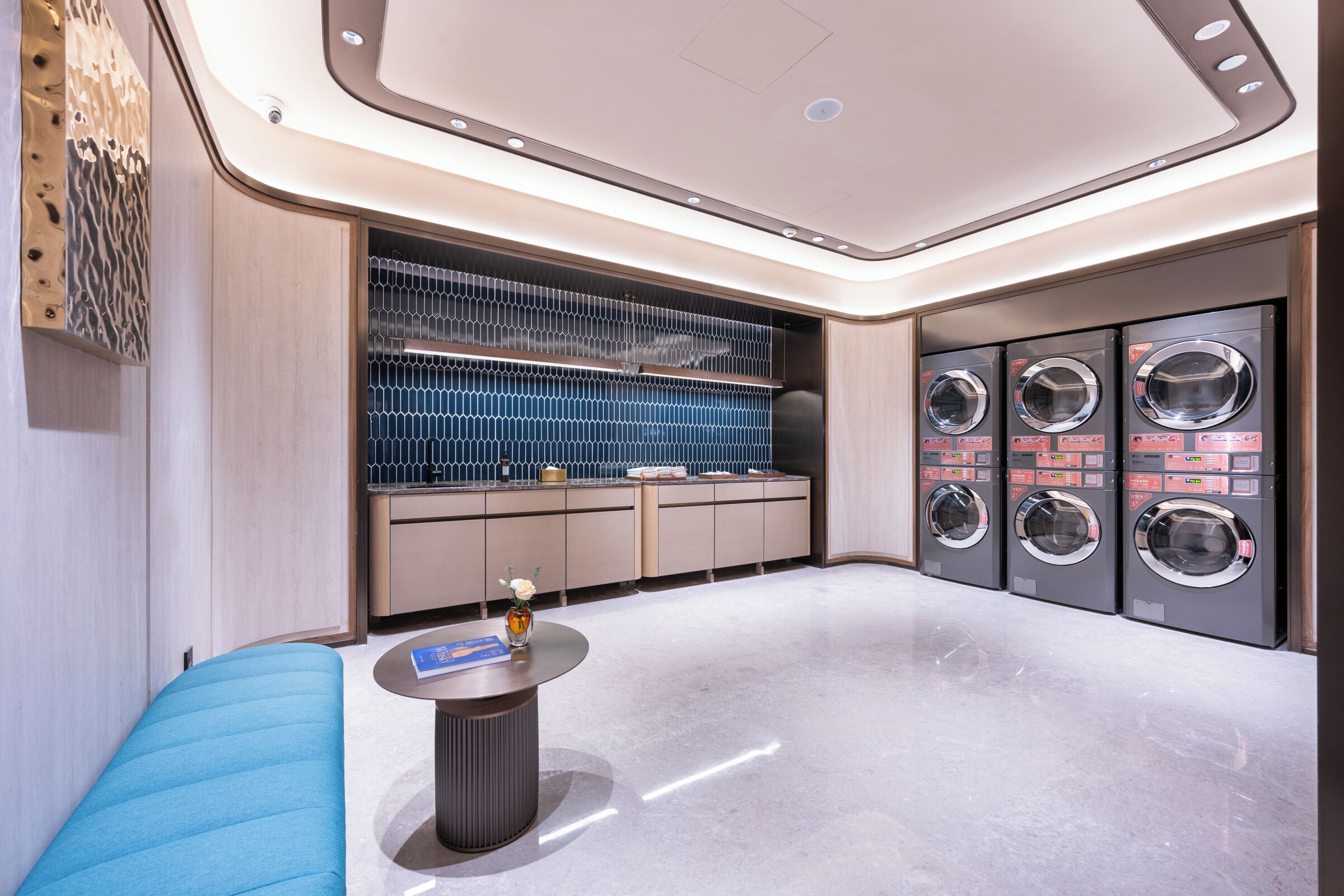 Een modern interieur met een zithoek, een kleine tafel met een vaas en een rij wasmachines.