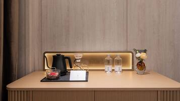 A wooden reception desk with a kettle, glass carafe, water bottles, a vase with flowers, and a card.