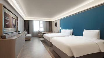 A hotel room with a TV, two beds, a sofa, a desk, and a large window.