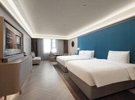 A hotel room with a TV, two beds, a sofa, a desk, and a large window.