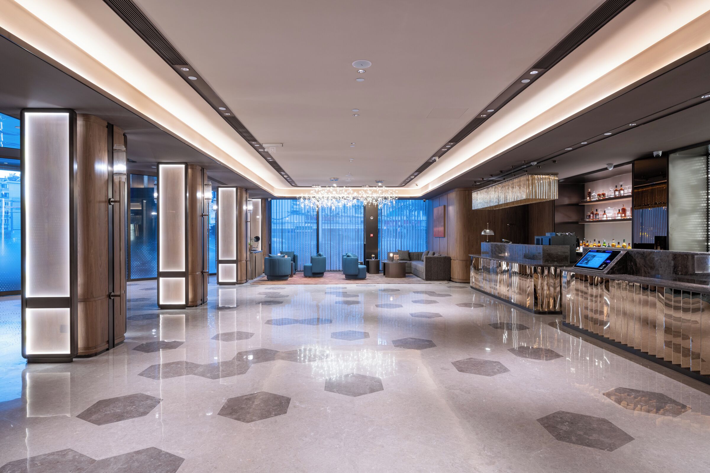Um lobby moderno com piso refletante, área de estar e bar com tela digital.