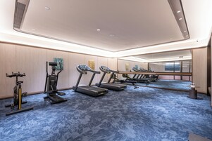 Habitación de hotel con un espejo grande, equipo de ejercicio que incluye una cinta de correr y una elíptica, y piso cubierto de alfombra azul.