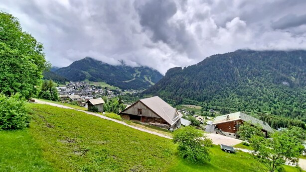 Un pueblo rural con casas de madera tradicionales, un camino sinuoso y montañas al fondo.