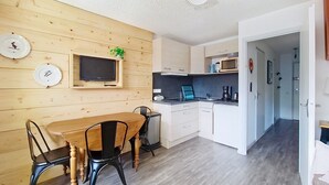 Cocina compacta con pared de madera, un televisor y un comedor con mesa y sillas.