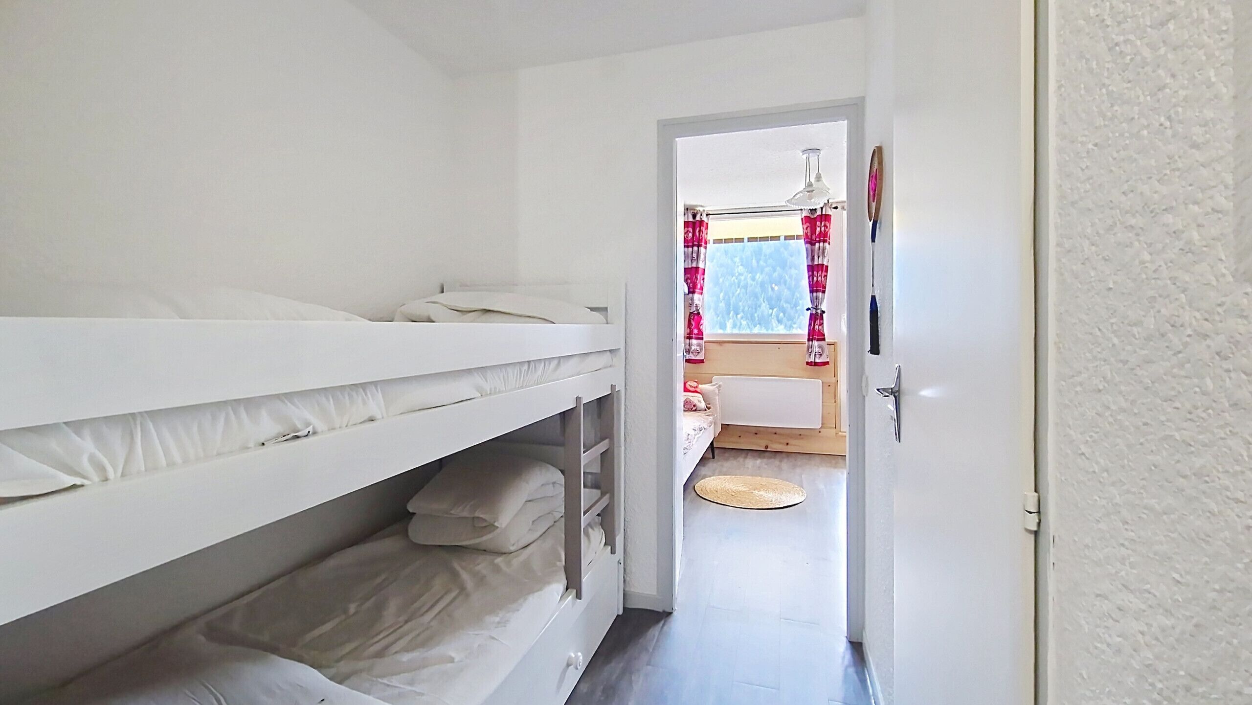 A room with a bunk bed, a door leading to a bathroom with a toilet and sink, and a window with curtains.