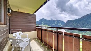 Ein Balkon mit Holzgeländer, zwei weiße Plastikstühle und Blick auf eine Berglandschaft.