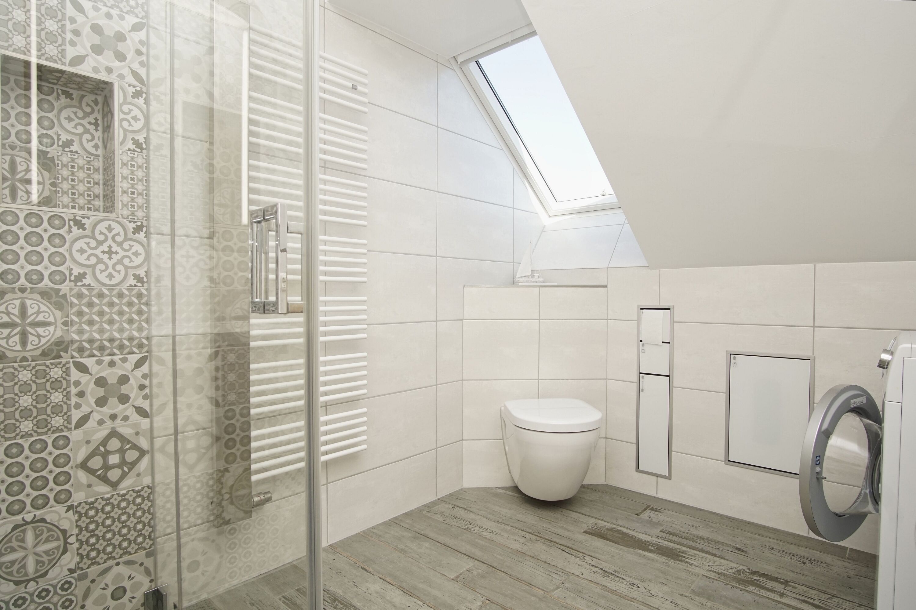 Ein modernes Badezimmer mit Dusche, Toilette und Waschmaschine, mit gemusterten Fliesen und einem Oberlicht.