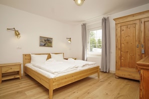 Ein Schlafzimmer mit einem hölzernen Bett, Nachttischen, einem Kleiderschrank und einem Fenster mit Vorhängen.