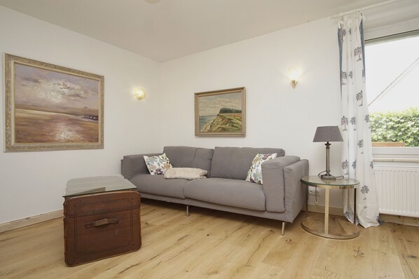 A room with a grey sofa, a glass-topped table, a lamp, a suitcase, and two paintings on the wall. - Surfer's Paradise Wiek - Holiday apartment Luv (Wiek)