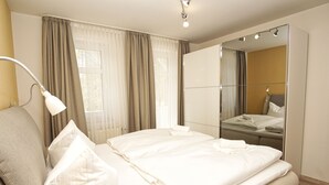 Une chambre d’hôtel avec un lit, une lampe de chevet, un miroir et une fenêtre avec des rideaux.