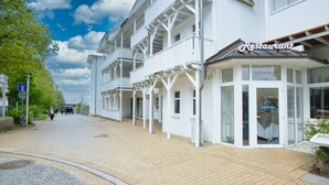 Un bâtiment blanc avec une enseigne indiquant la présence d’un restaurant, une allée couverte et un ciel dégagé.