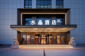 A hotel entrance with a modern design, featuring a prominent sign, a covered entrance, and two stone lion statues. - Crystal Hotel Qingdao May Fourth Square (Qingdao)