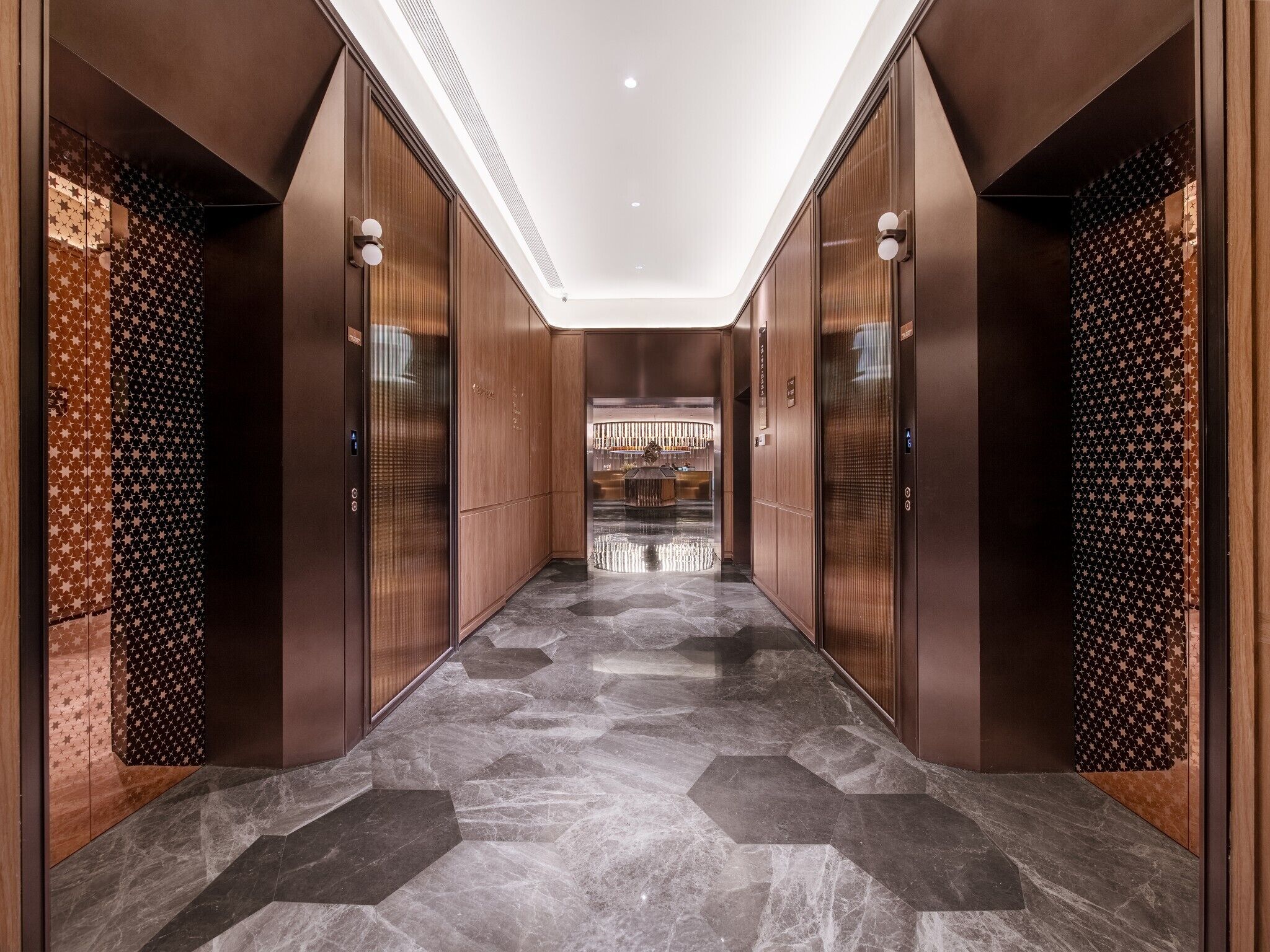 A modern hallway with a geometric patterned floor, wooden paneling, and a central elevator.