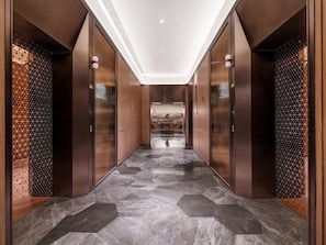 A modern hallway with a geometric patterned floor, wooden paneling, and a central elevator. - Crystal Hotel Qingdao May Fourth Square (Qingdao)