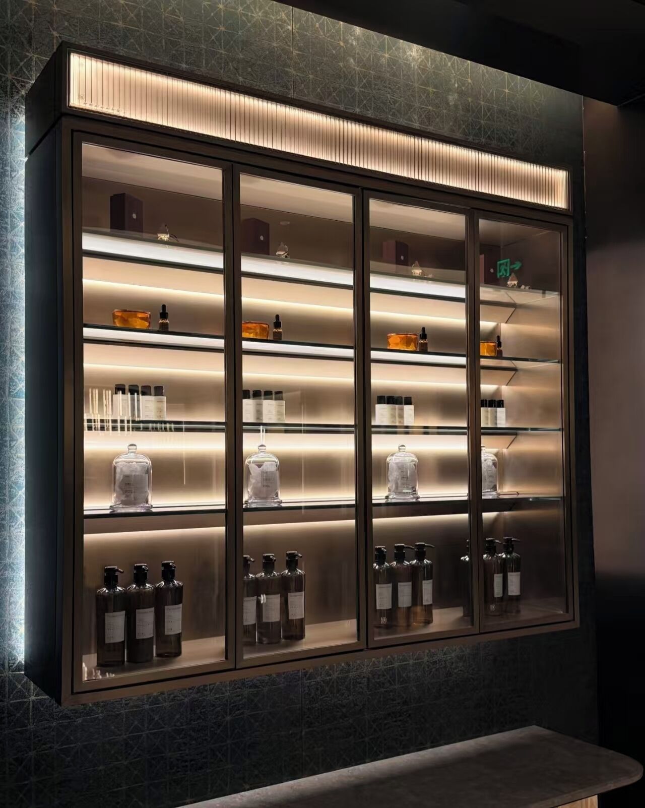 A modern, well-lit display cabinet with multiple shelves containing various bottles and containers.