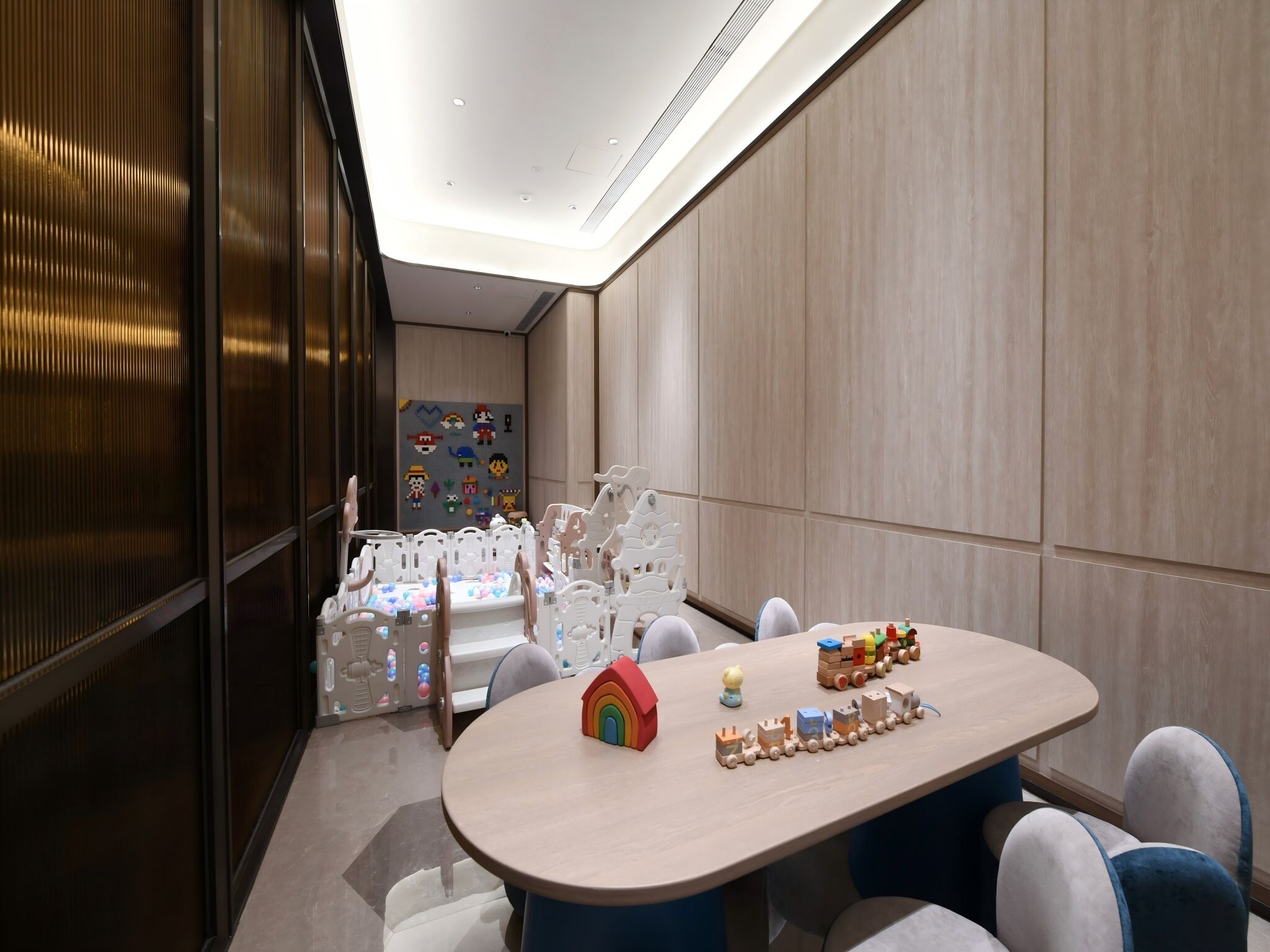 Un espace de jeux pour enfants avec une piscine à balles, un mur décoré sur le thème de Mario et une table en bois avec des trains miniatures.