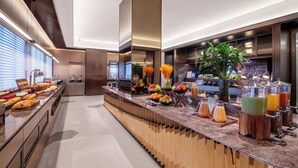 Un mostrador de desayuno moderno en un hotel, con una variedad de frutas, una barra de zumos y una planta grande.