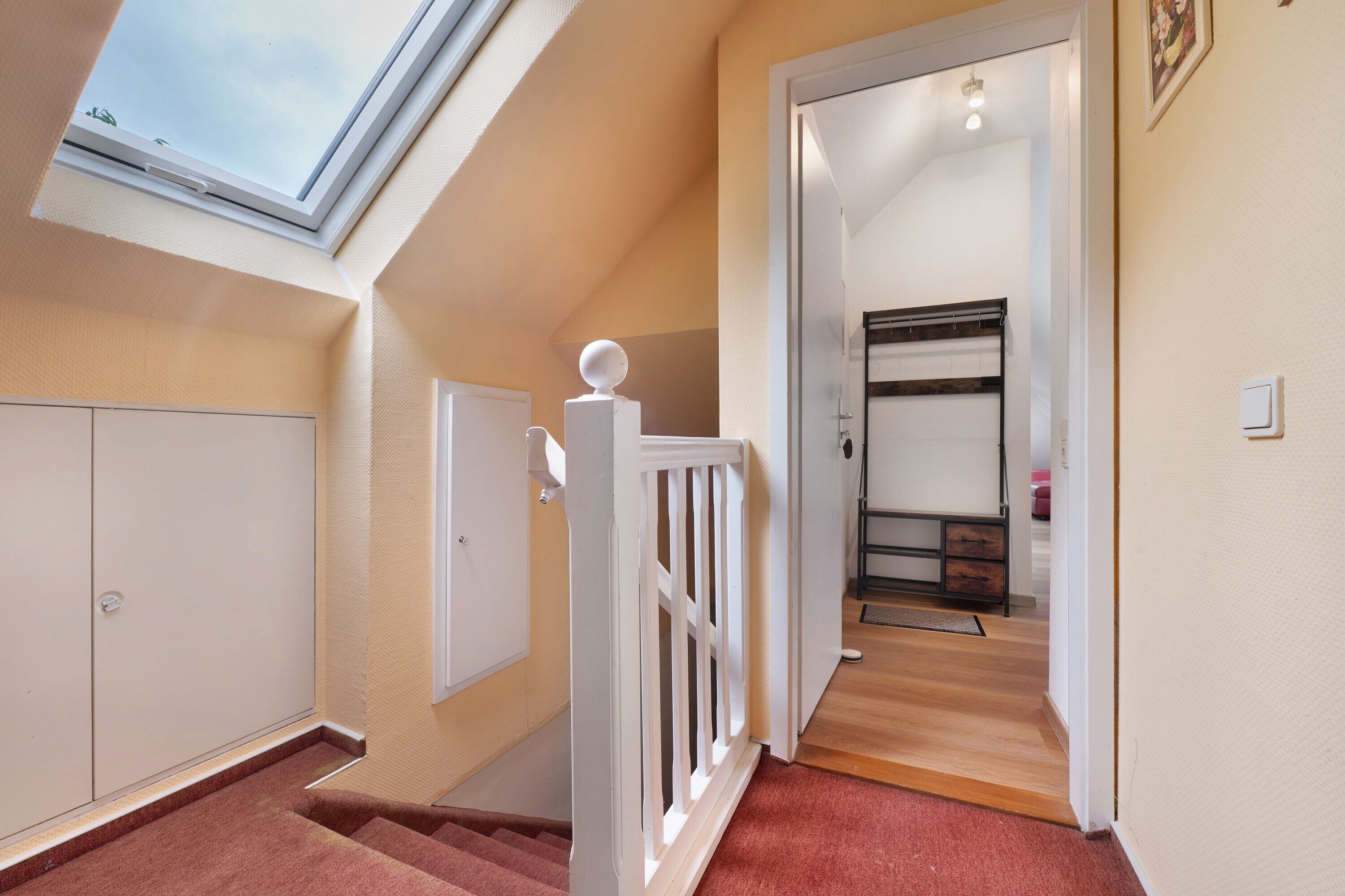 A staircase with a white railing, a skylight, and a view into a room with a bed and a dresser.