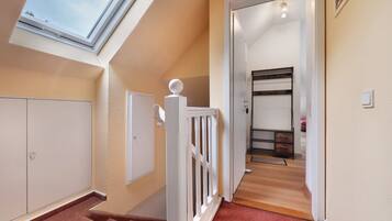 A staircase with a white railing, a skylight, and a view into a room with a bed and a dresser.