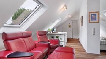 Une chambre de style loft moderne, avec un plafond en pente, un coin salon en cuir rouge, une petite kitchenette et une vue sur le ciel grâce à une lucarne.