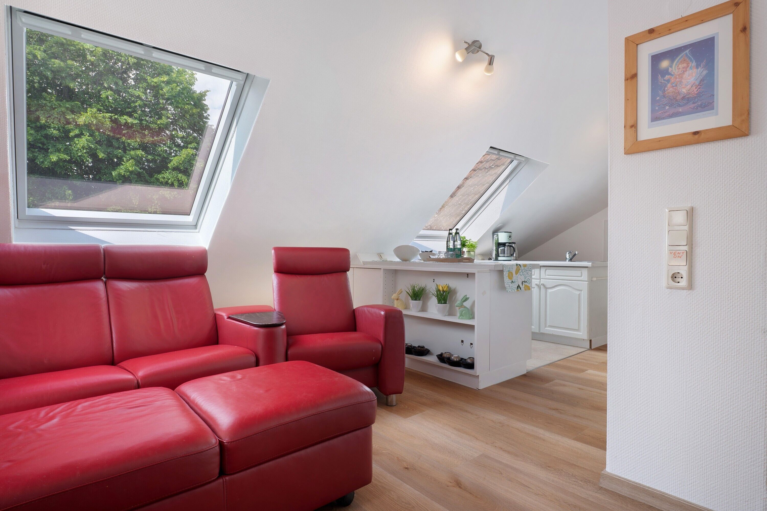 Een moderne kamer met een rode bank, een tafeltje, een keukenhoek en een dakraam.