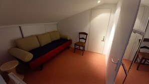 Quarto com sofá vermelho, cadeira de madeira, porta branca e pequena mesa com cadeira.
