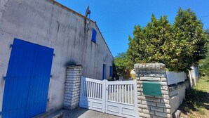 Un edificio con puerta azul, portón blanco y pared de piedra con placa numérica.