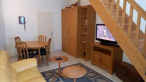 Uma sala de estar com sofá, mesa de jantar com cadeiras, televisão, armários de madeira e escada.