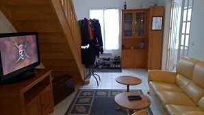 Una sala de estar con televisor, sofá, una mesita, escalera, armario y zapatero.
