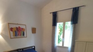 Un dormitorio con cama, ventana con cortinas, una puerta y una lámpara fijada a la pared.