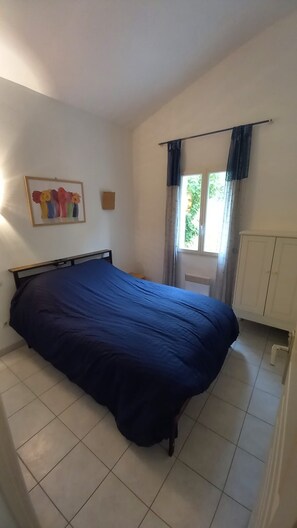 Ein Schlafzimmer mit Bett, einem Fenster mit Vorhängen, einer Tür und einer Wandleuchte.