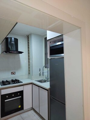 Una cocina equipada con estufa a gas, horno, refrigerador de acero inoxidable y extractor de aire negro.