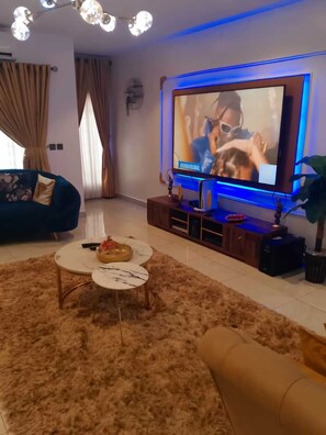 Una sala de estar con un televisor de pantalla plana grande, un sofá, una mesa de centro y una planta decorativa.