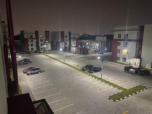 Un estacionamiento con varios autos, un edificio de fachada roja y blanca, y una entrada bien iluminada.