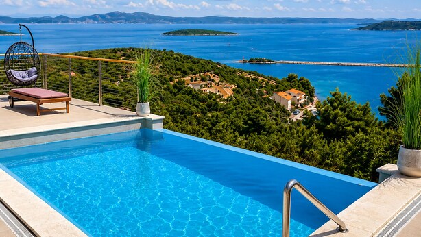 A pool with a view of a coastal landscape, a lounge chair, and a hanging chair.