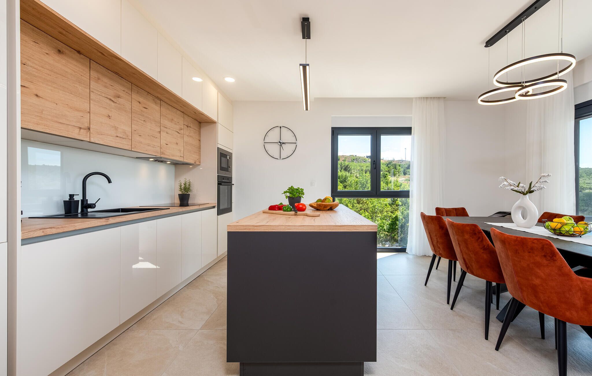 Uma cozinha moderna com uma ilha central, armários de madeira e um espaço de refeições com cadeiras laranjas.