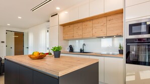 Cozinha moderna com ilha de madeira, armários brancos e eletrodomésticos de aço inoxidável.