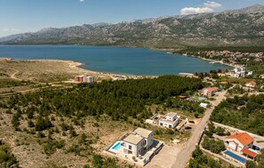 A coastal area with a large body of water, mountainous terrain in the background, and a residential area with houses and a swimming pool. - Gorgeous home in Rovanjska (Rovanjska)