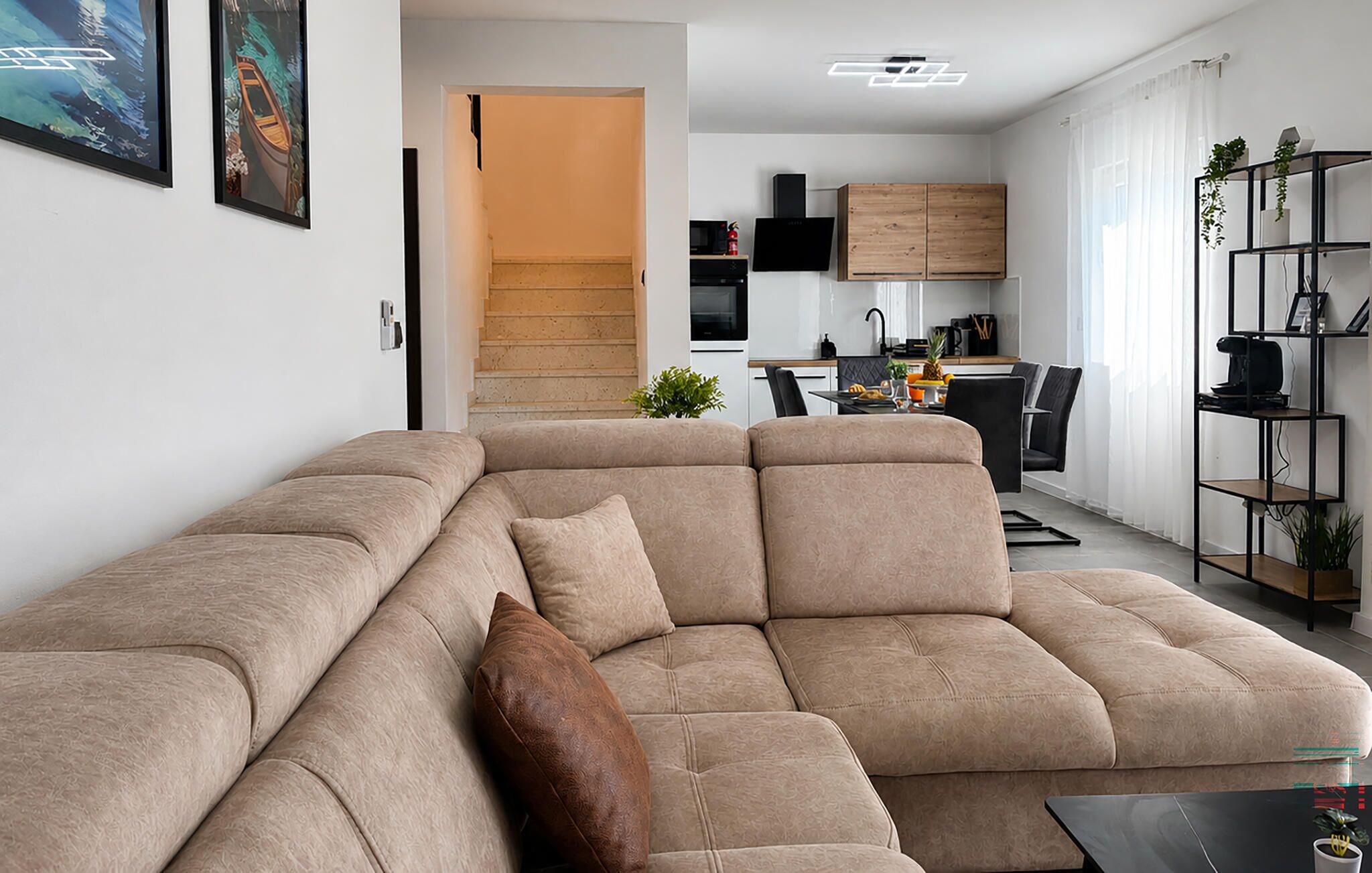 Ein modernes Wohnzimmer mit einem Ecksofa, einem Essbereich und einer Küche im Hintergrund.