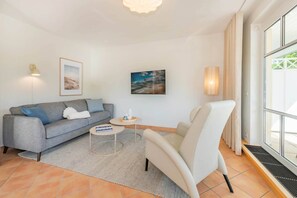 Ein Wohnzimmer mit grauem Sofa, weißem Sessel, kleinem runden Tisch und zwei Wandleuchten.