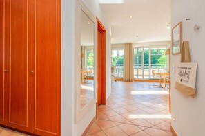 Ein Hotelgang mit Holztüren, Fliesenboden und Blick auf einen Außenbereich mit Sitzgelegenheiten.