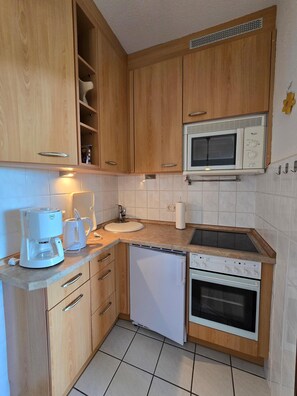 A compact kitchen with wooden cabinets, a microwave, a coffee maker, a sink, and a dishwasher. - Four Seasons 2-49 - Großenbrode (Großenbrode)