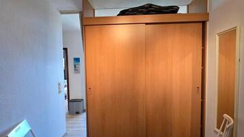 Ein Zimmer mit Holzschrank, einem Sessel, einem Schreibtisch mit Laptop und einem Bett.