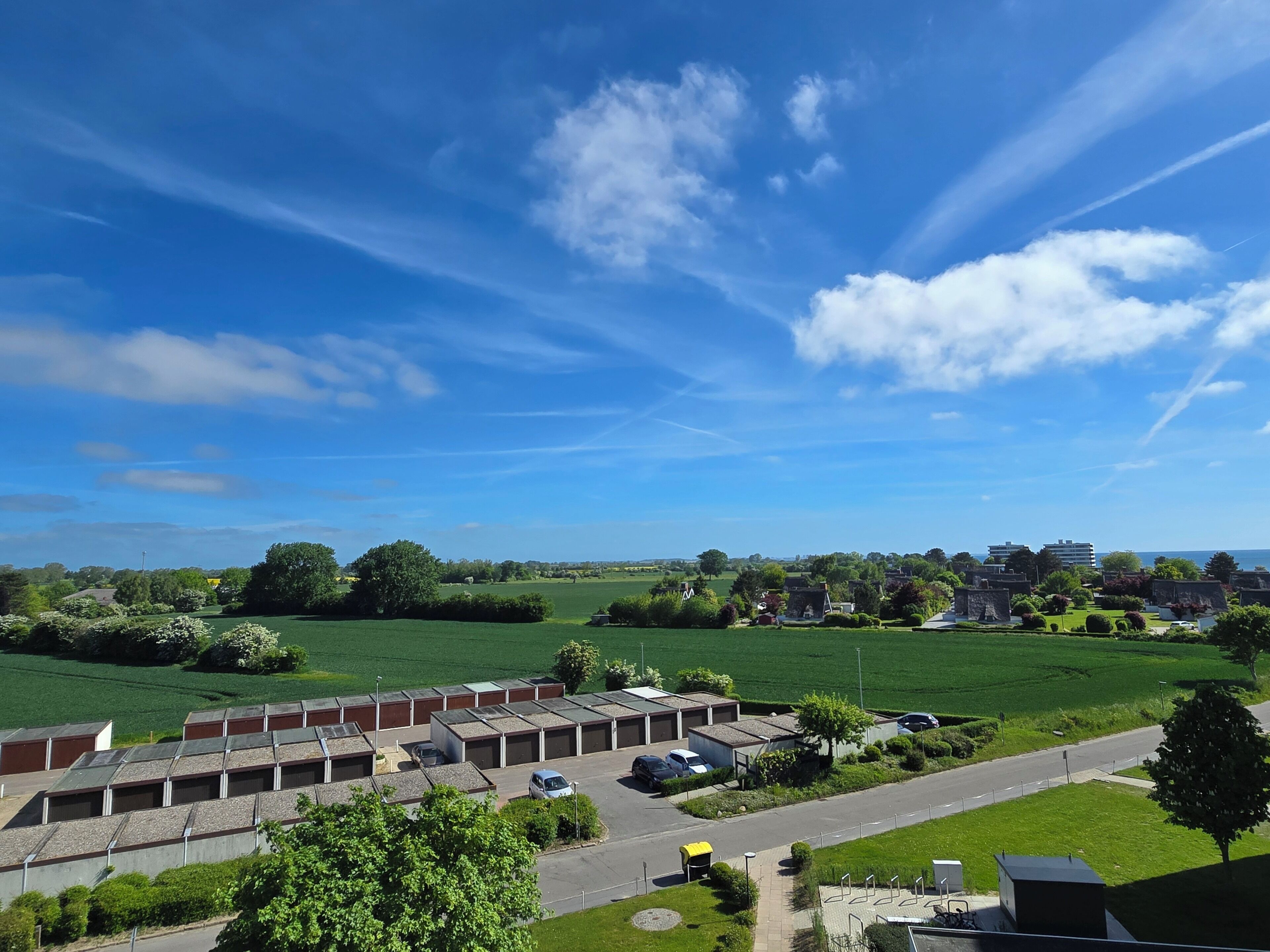 A residential area with a row of detached houses, a green field, and a clear blue sky.